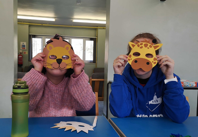 Staff and member holding hand made animal masks on their face.