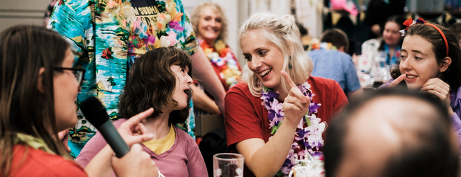 Photo of member and staff laughing together whilst wearing flower necklaces.