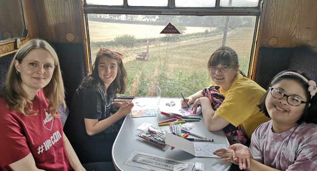 Group of young people on a train by the window and colouring in activity sheets.