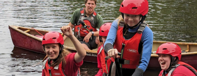 4 people balancing on kayaks on a river laughing